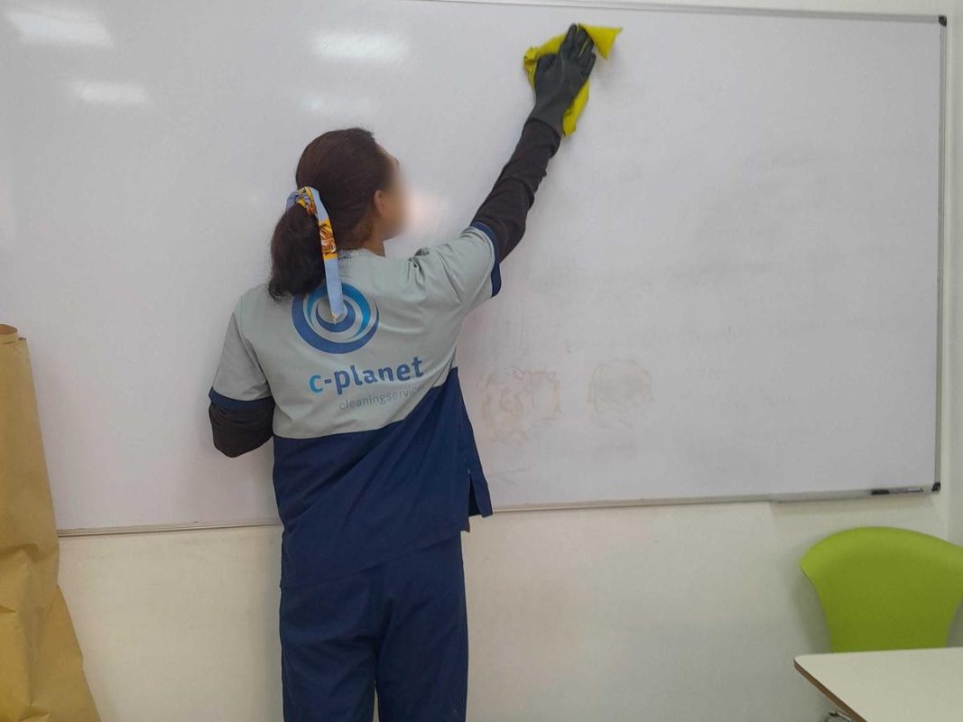 Personal de C-Planet con uniforme limpiando el pizarrón de un aula