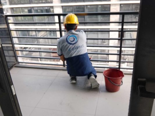 Operario de C-Planet con casco limpiando el balcón de un edificio nuevo en una limpieza final de obra